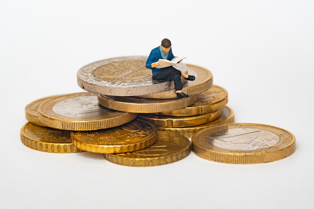 Miniature figure sitting on coin stack reading newspaper representing budget hosting decisions